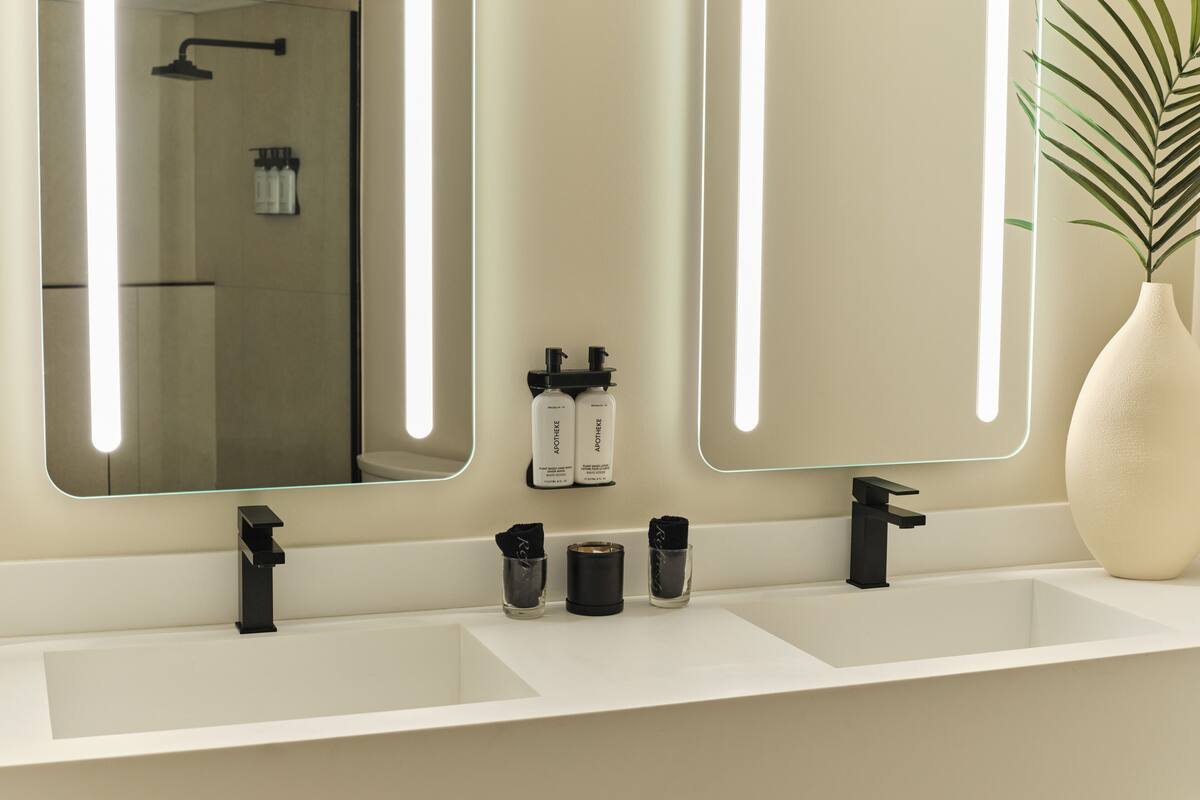 A modern bathroom with two sinks, a large mirror, and a potted plant.
