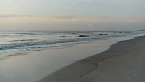 Une plage avec des vagues, une jetée au loin et un ciel dégagé.