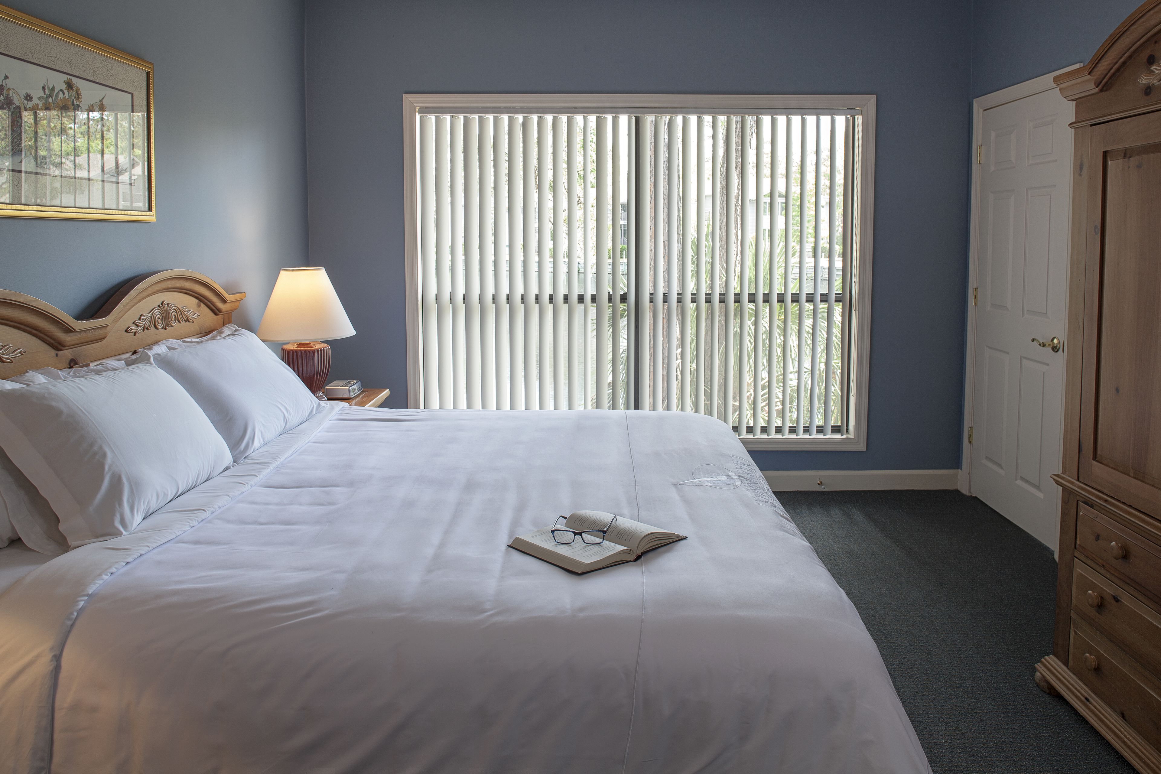 A neatly made bed with white linens, a bedside lamp, and a book with glasses on it.