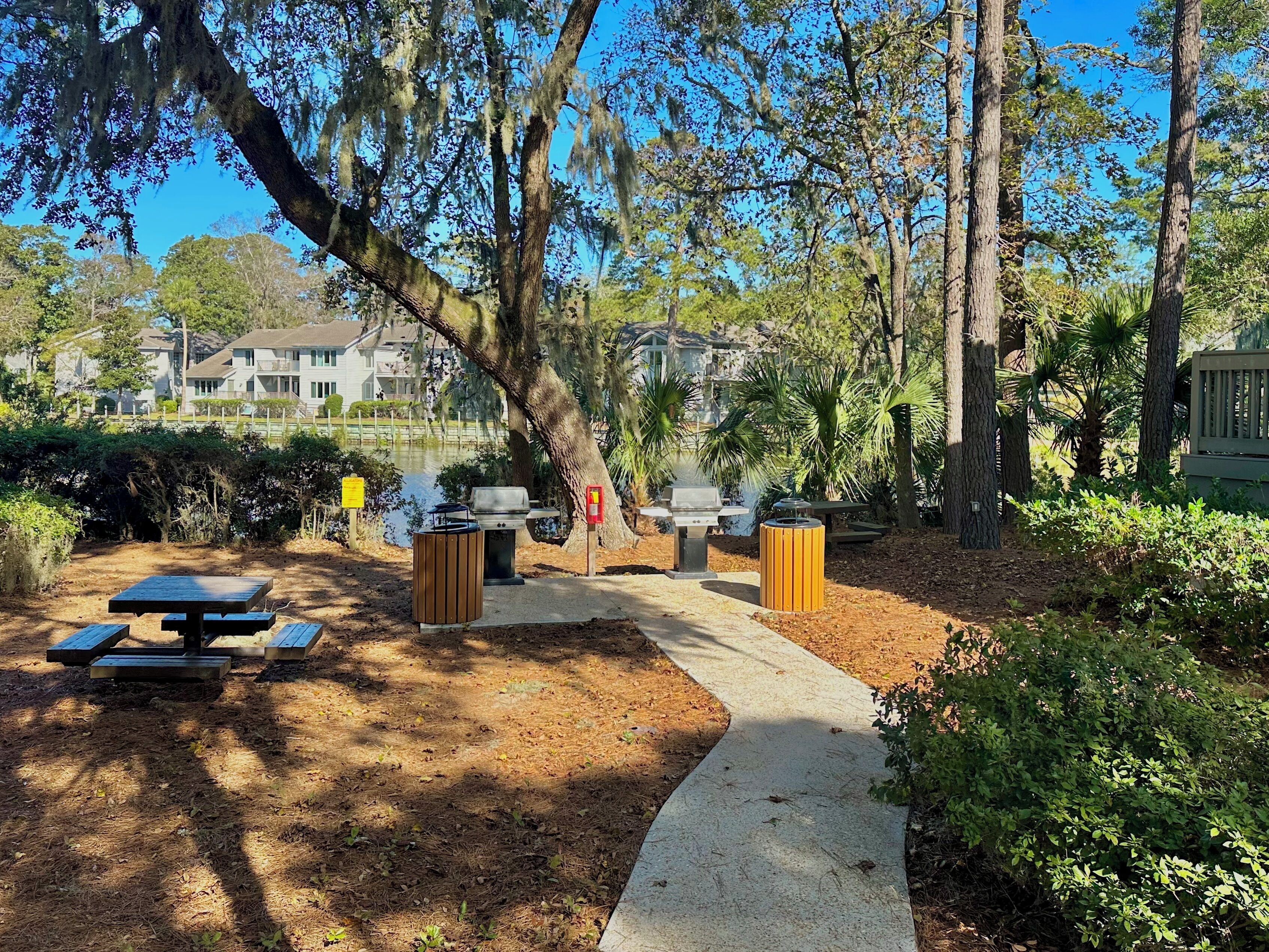 A picnic area with a grill, benches, and a trash can.