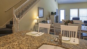 Un comedor con encimera de granito, sillas blancas y una mesa.