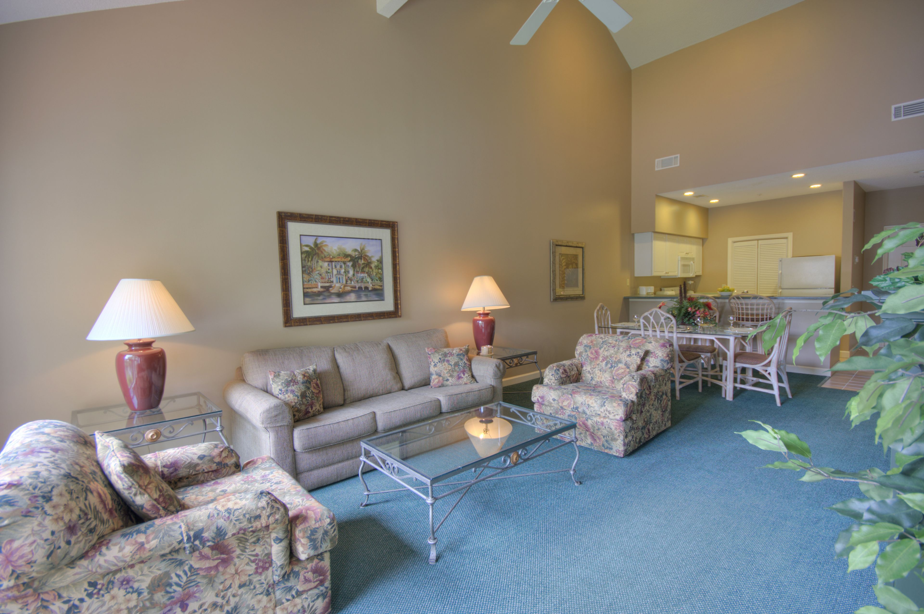 A living room with a sofa, armchairs, a coffee table, and lamps. There is a dining area with a table and chairs.