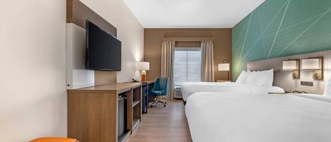 A hotel room with a bed, a desk with a TV, a chair, and a window with curtains.
