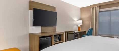 Une chambre d’hôtel équipée d’un lit, d’une télévision, d’un four à micro-ondes, d’un bureau, d’une chaise et d’une fenêtre avec des rideaux.