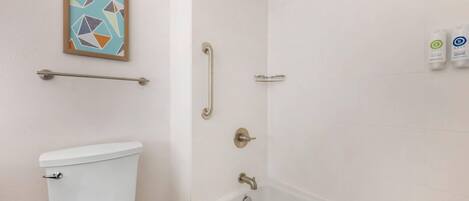A bathroom with a toilet, a shower with grab bars, and a bathtub.