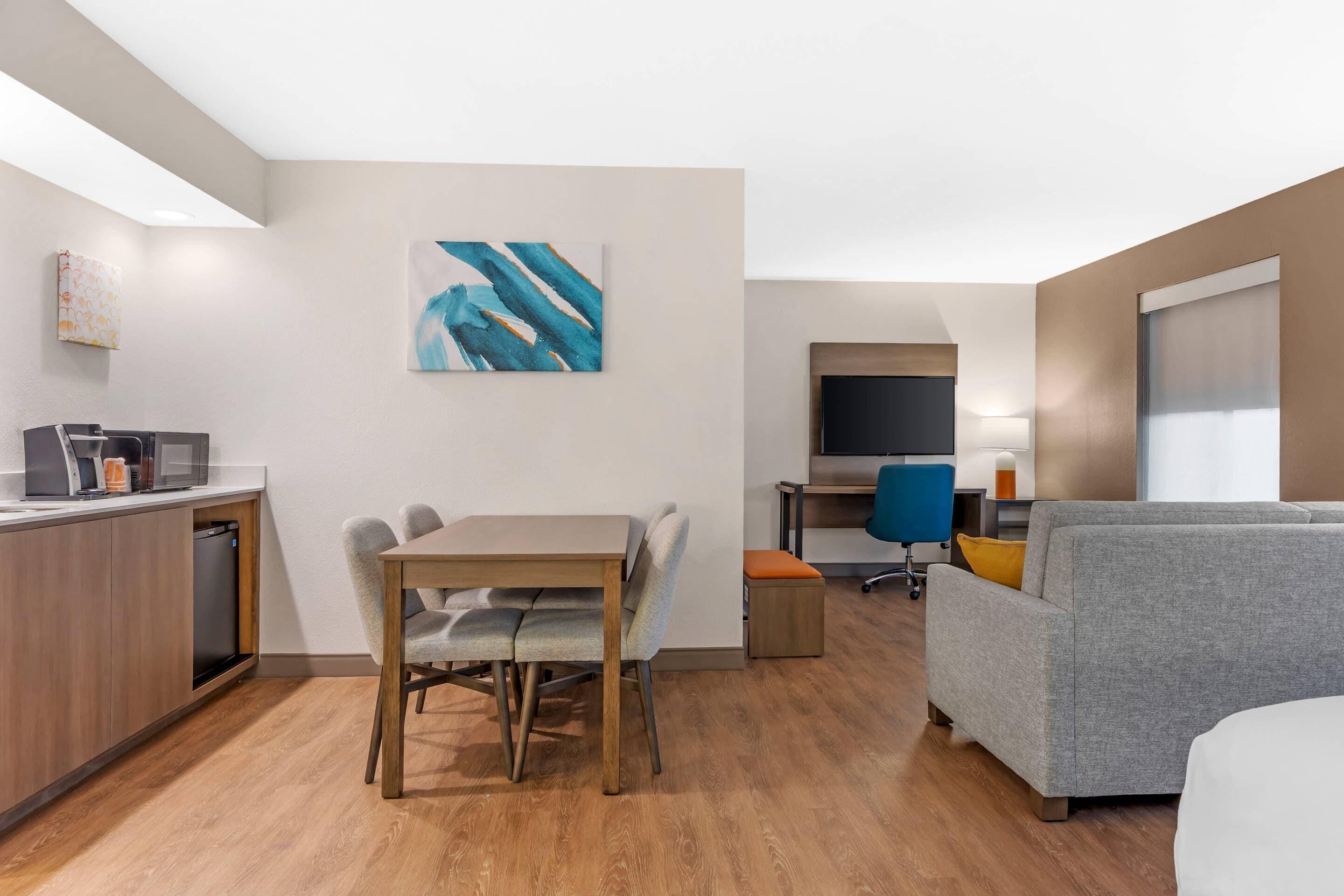 A modern living room with a grey sofa, a wooden dining table, and a kitchen area with a dishwasher.