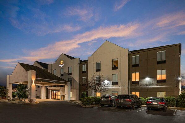 A hotel with a modern design, featuring a central entrance, multiple parking spaces, and a well-lit facade.