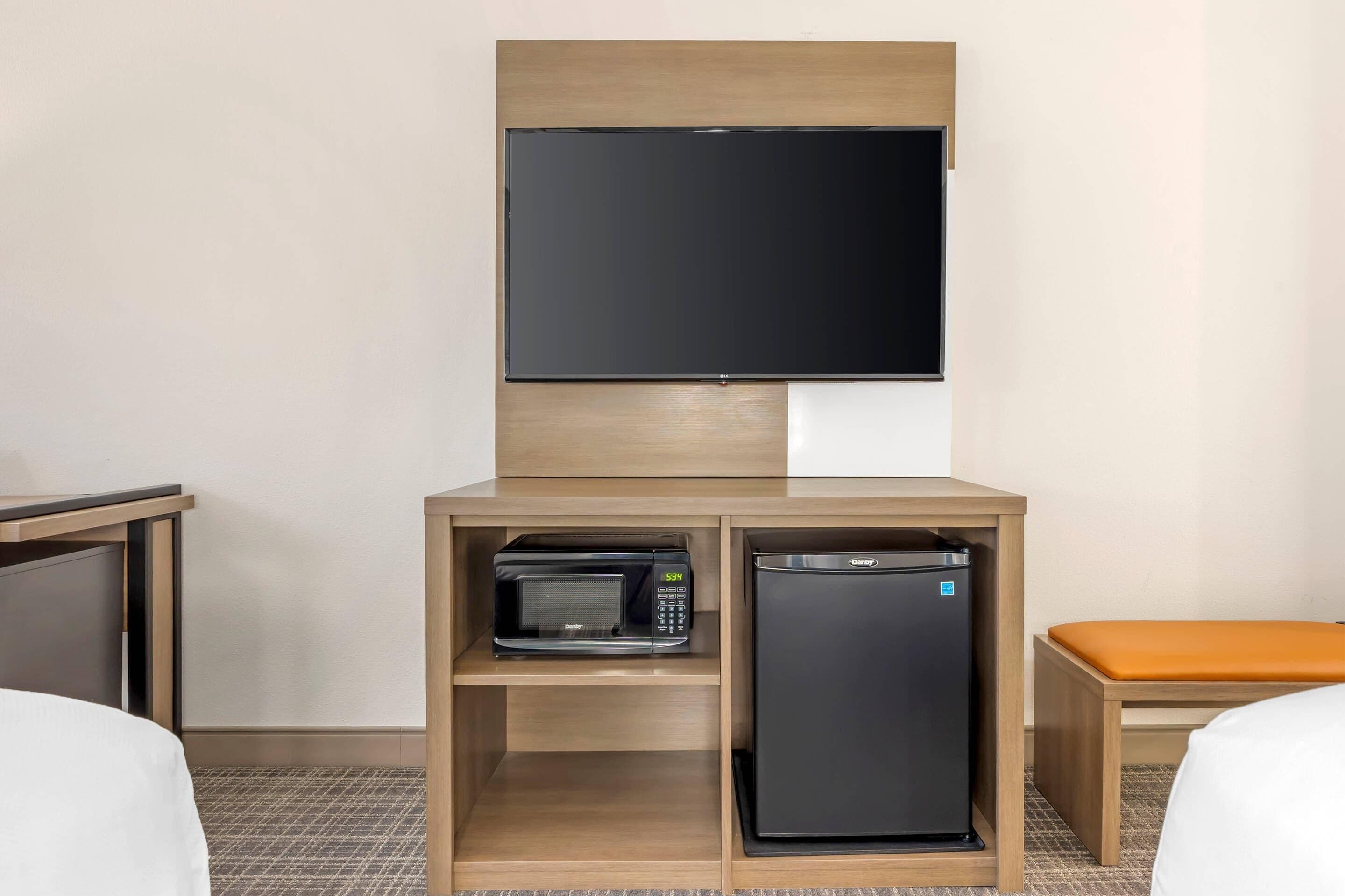 Habitación de hotel con televisor de pantalla plana sobre un mueble de madera que contiene un microondas y un refrigerador pequeño.