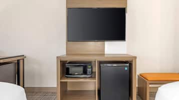 Habitación de hotel con televisor de pantalla plana sobre un mueble de madera que contiene un microondas y un refrigerador pequeño.