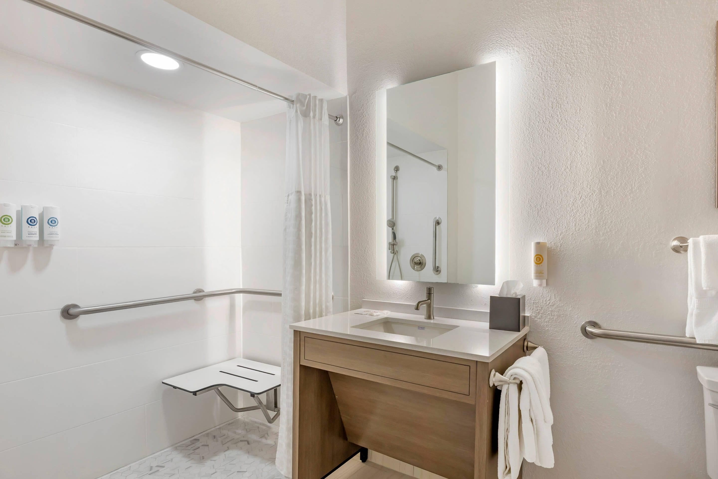 Een moderne badkamer met een douche, wastafel, spiegel en handgrepen.