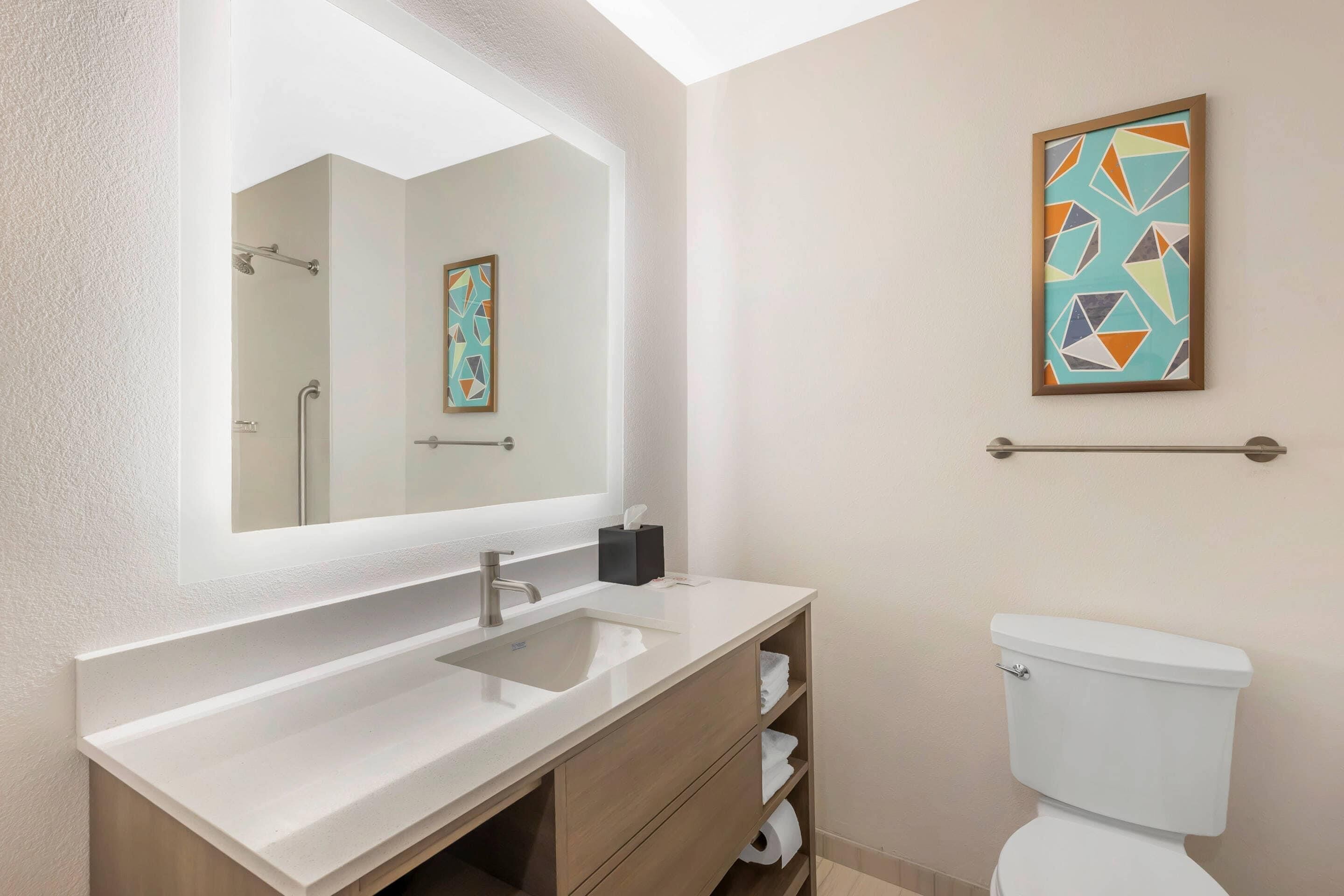 Un bany modern amb un mirall gran, un lavabo, un vàter i una barra de tovalloles.