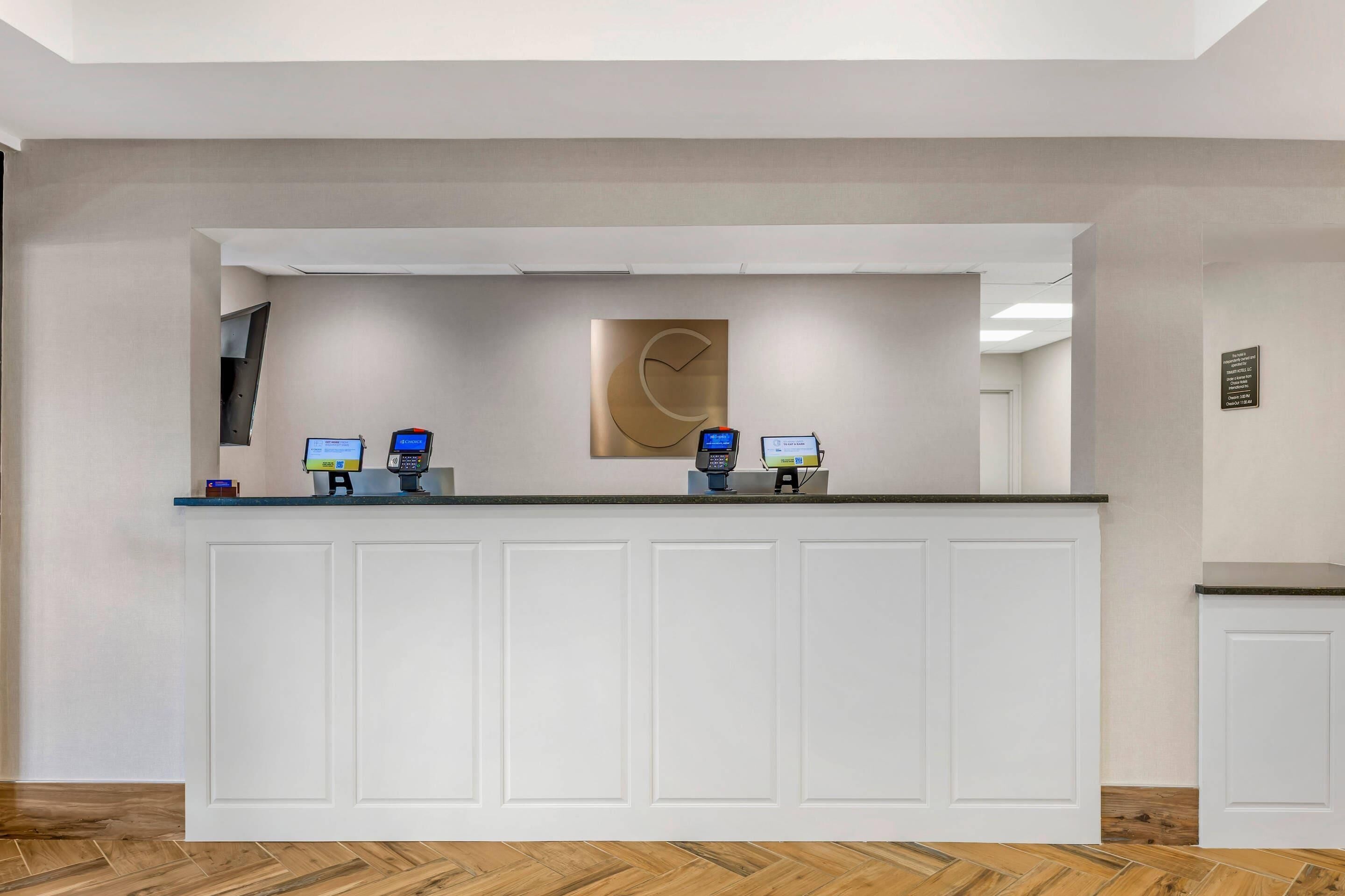 A reception desk with two computer monitors, a cash register, and a wall-mounted clock.