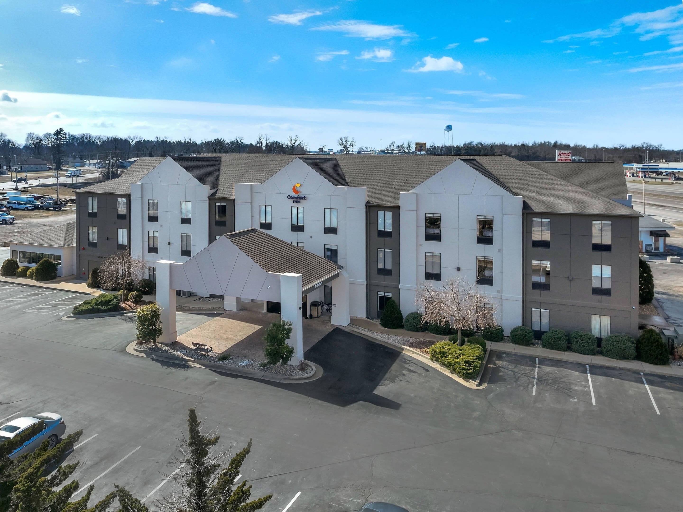 A multi-story hotel with a central entrance, parking lot, and a clear view of the surrounding area.