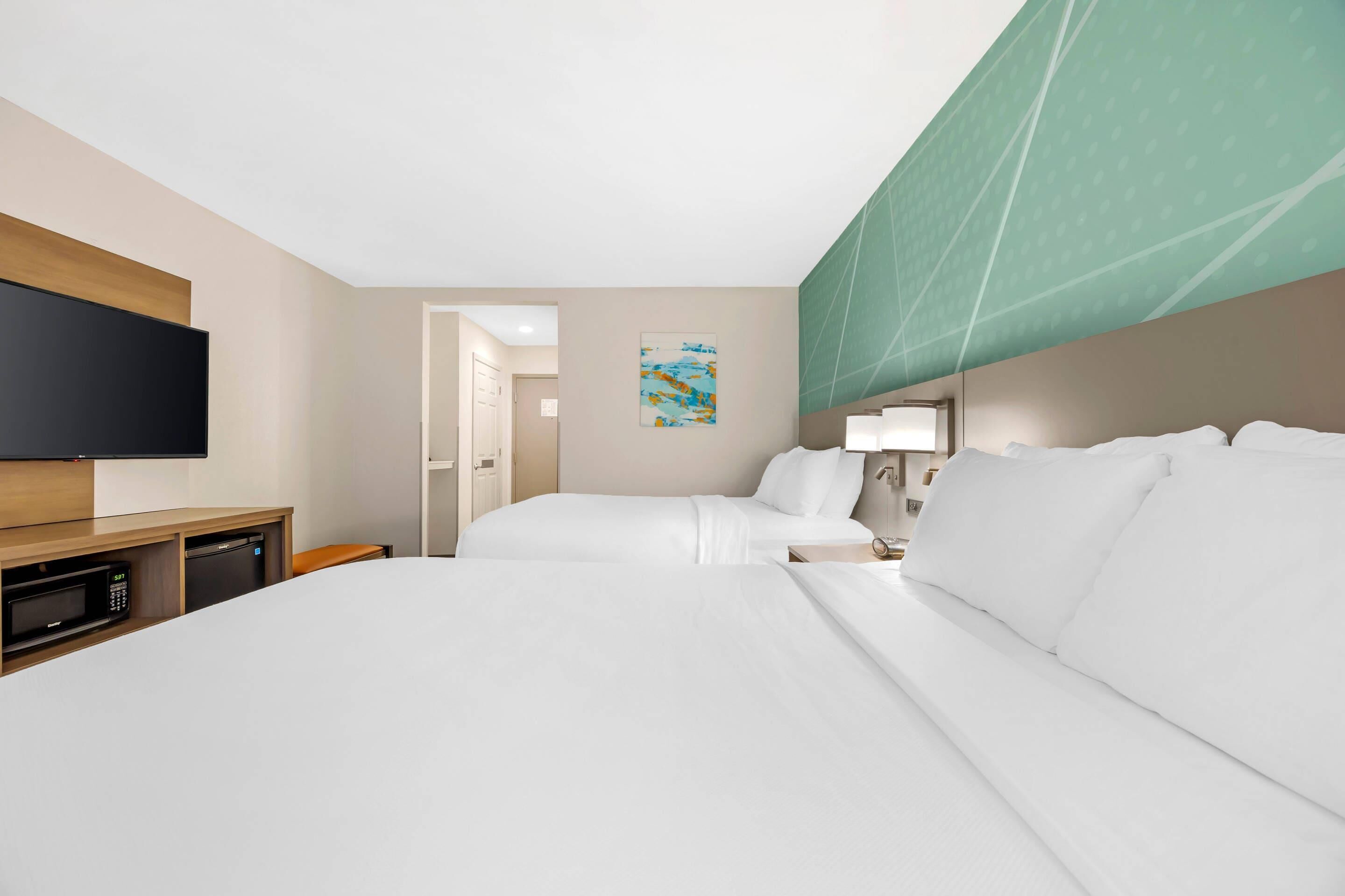 A hotel room with two beds, a flat-screen TV, a microwave, and a small desk.