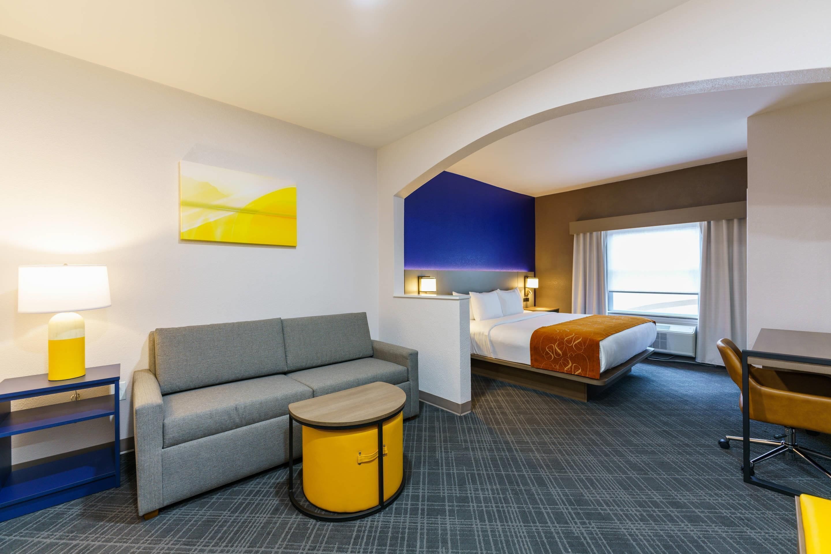Una habitación de hotel con cama, sofá, una mesita, escritorio y lámpara.