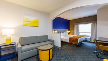Una habitación de hotel con cama, sofá, una mesita, escritorio y lámpara.