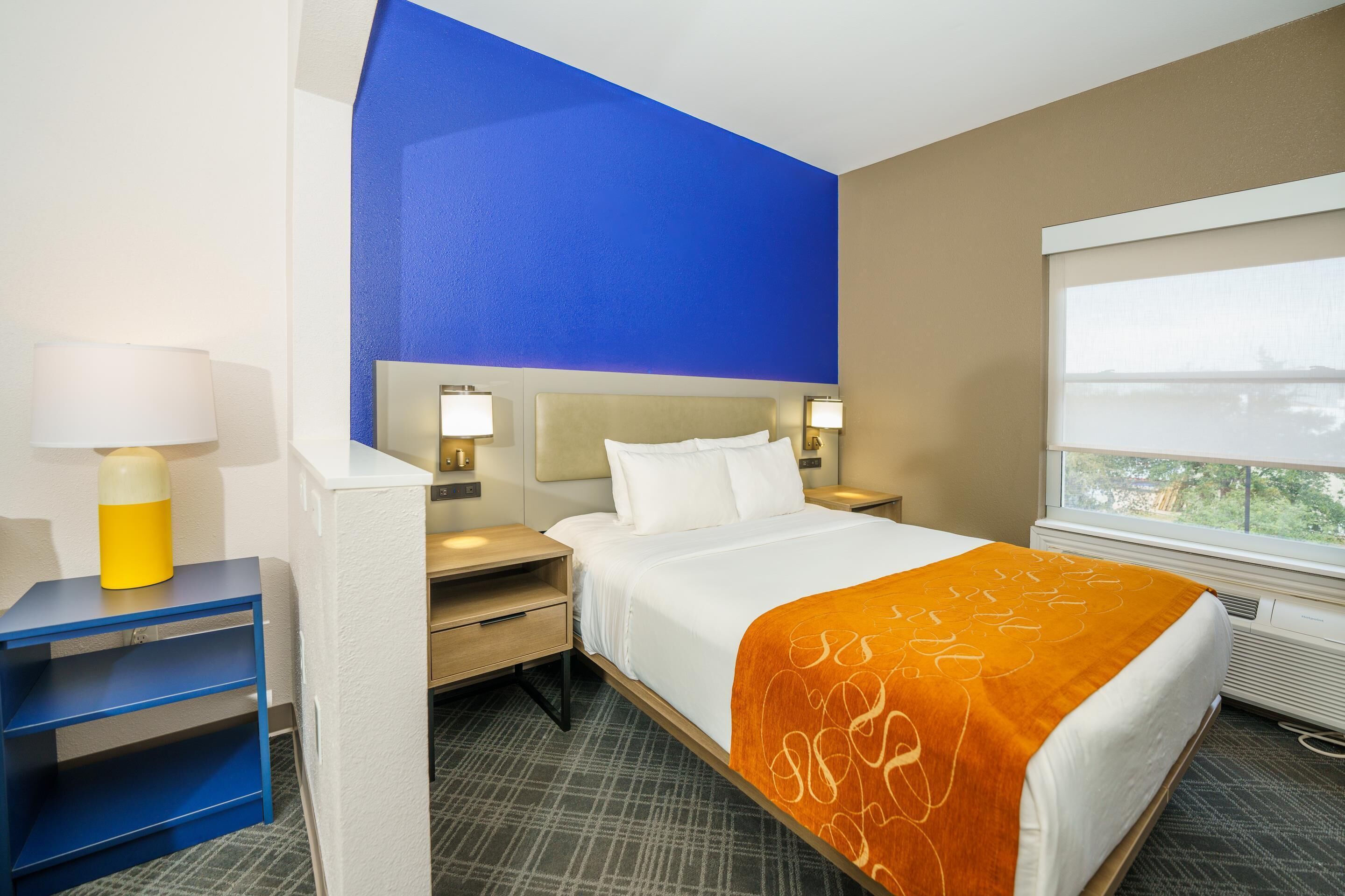 A hotel room with a bed, nightstands, a lamp, and a window with a view.