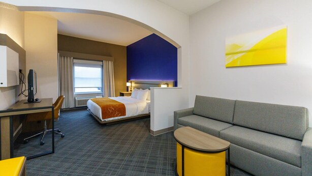 A hotel room with a bed, a desk, a sofa, and a small table. - Comfort Suites University Drive (College Station)
