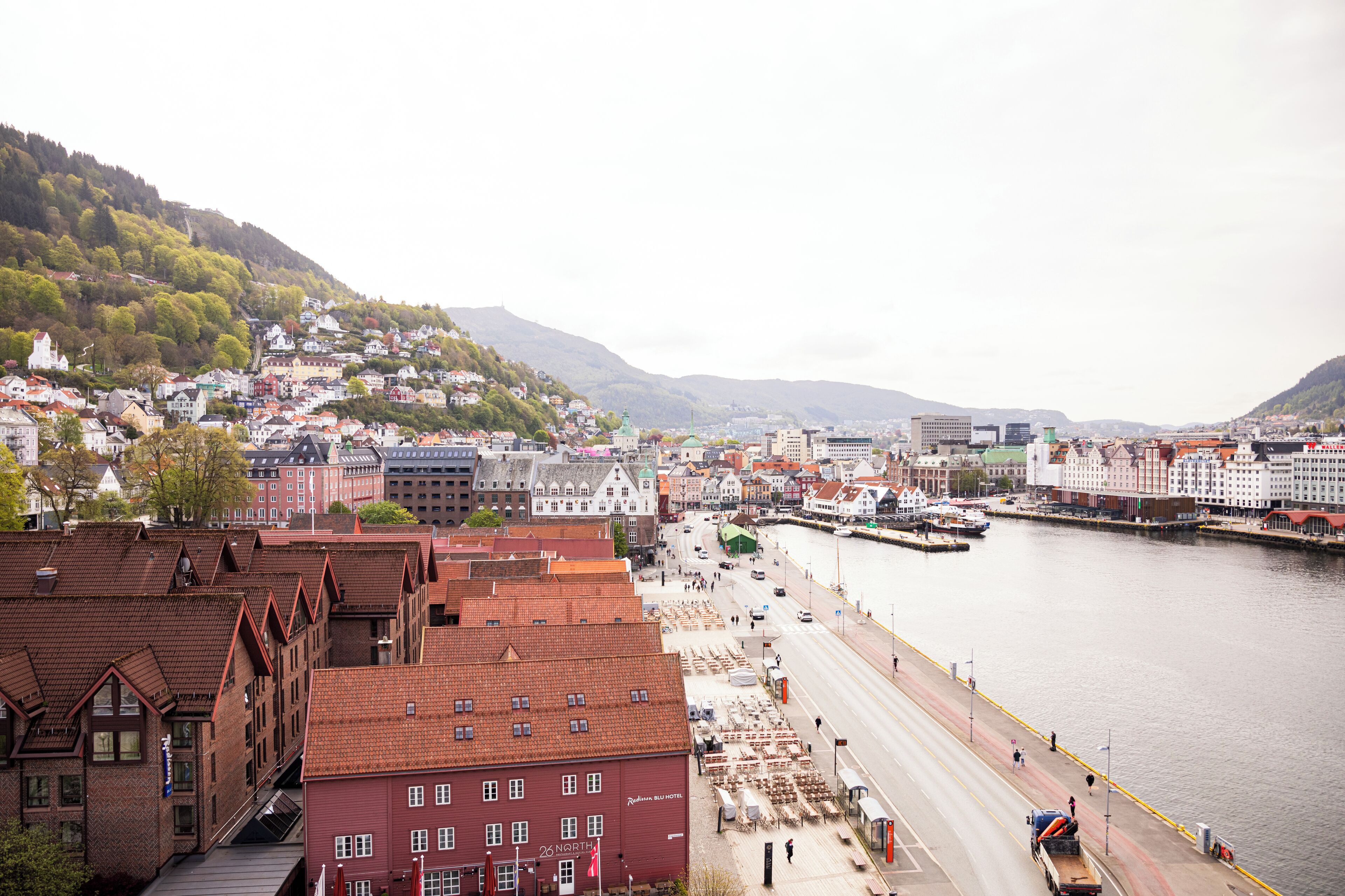 A riverside town with buildings along the water, a bridge, and a hilly backdrop.