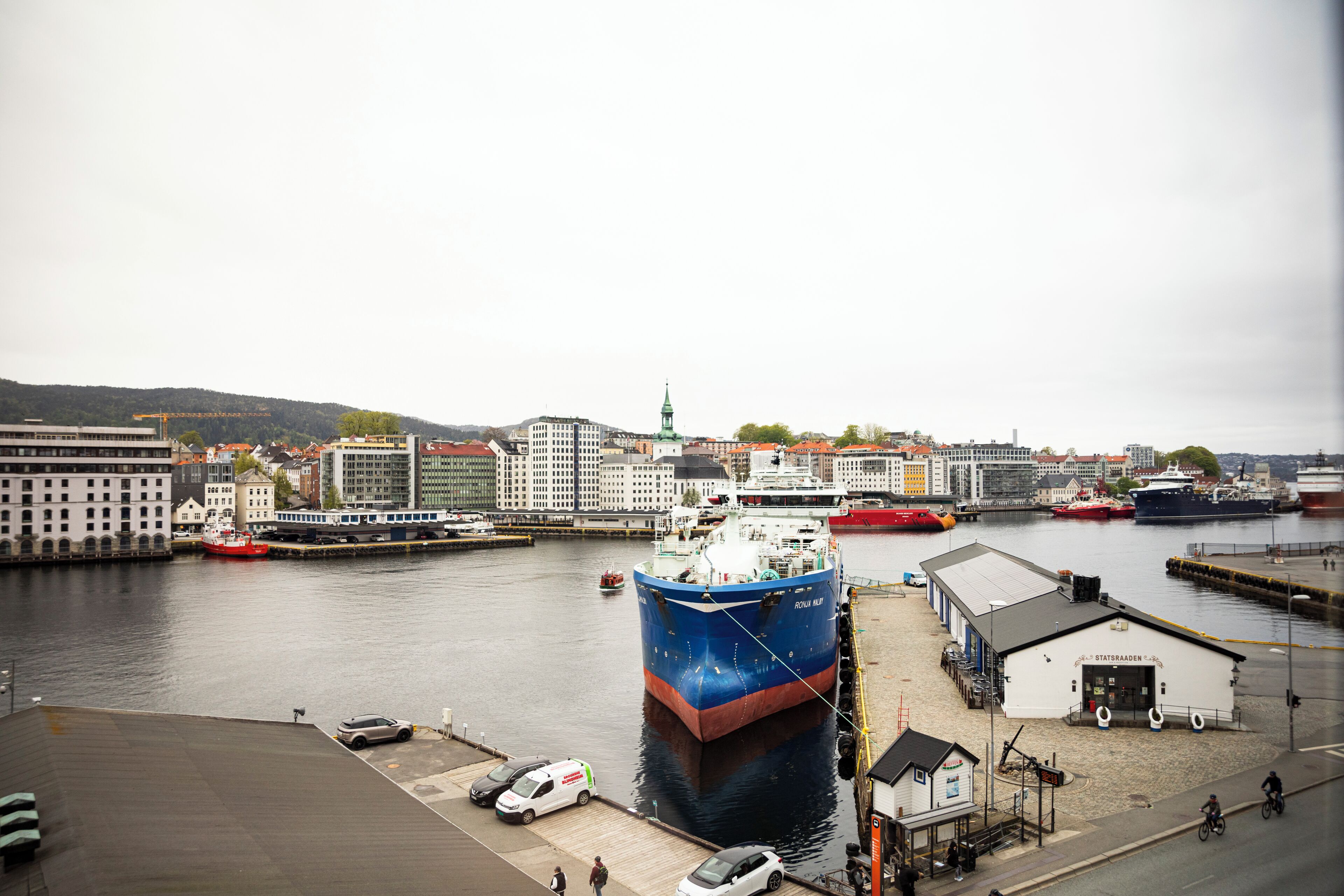 A harbor with a large blue ship docked, a white building with a sign, and a small white structure with a sign.