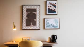 A room with a round table, a yellow chair, a lamp, and framed pictures on the wall.