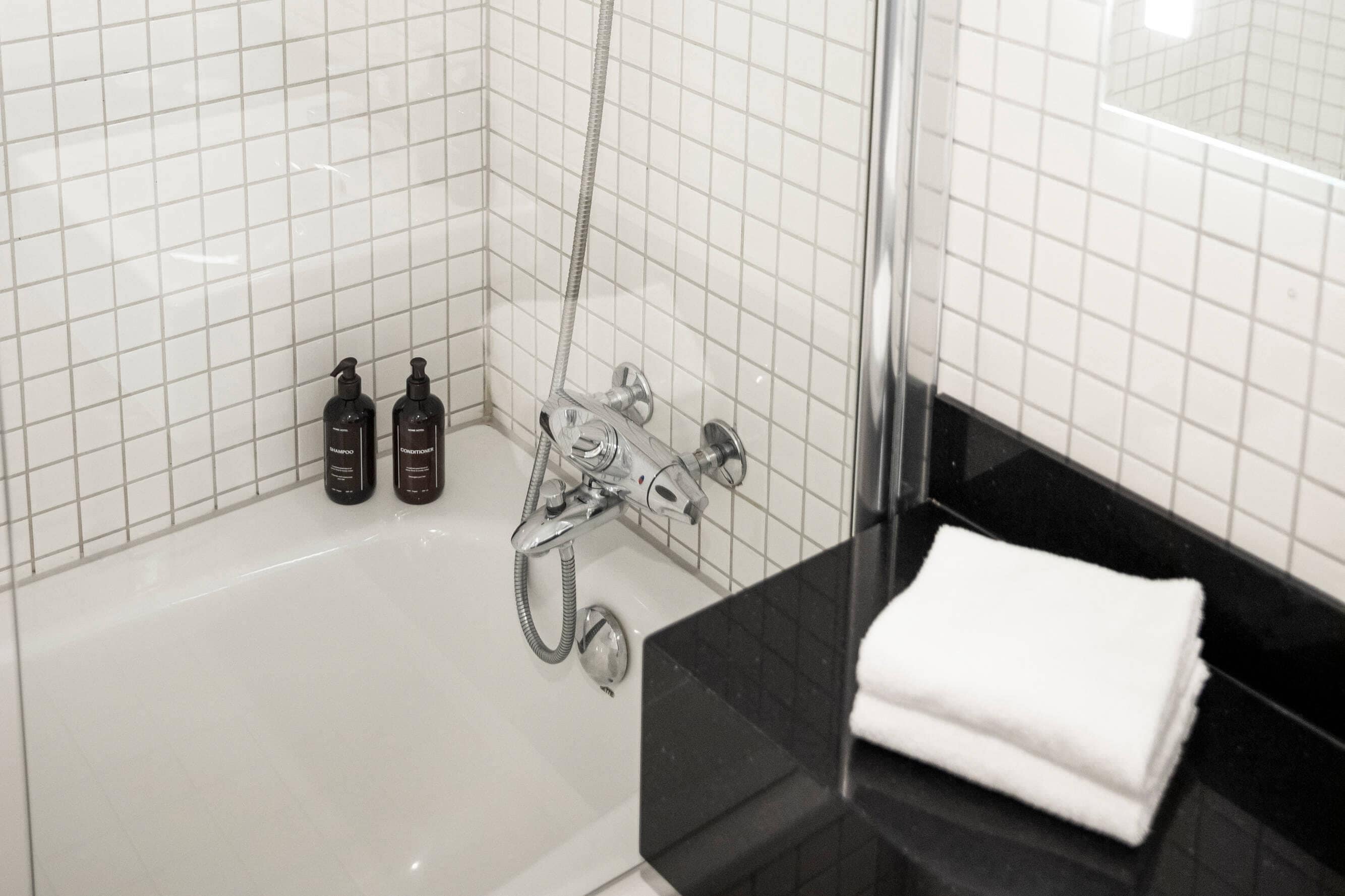 Une salle de bain avec une douche carrelée de carreaux blancs, un plan de toilette noir et trois bouteilles de shampoing.