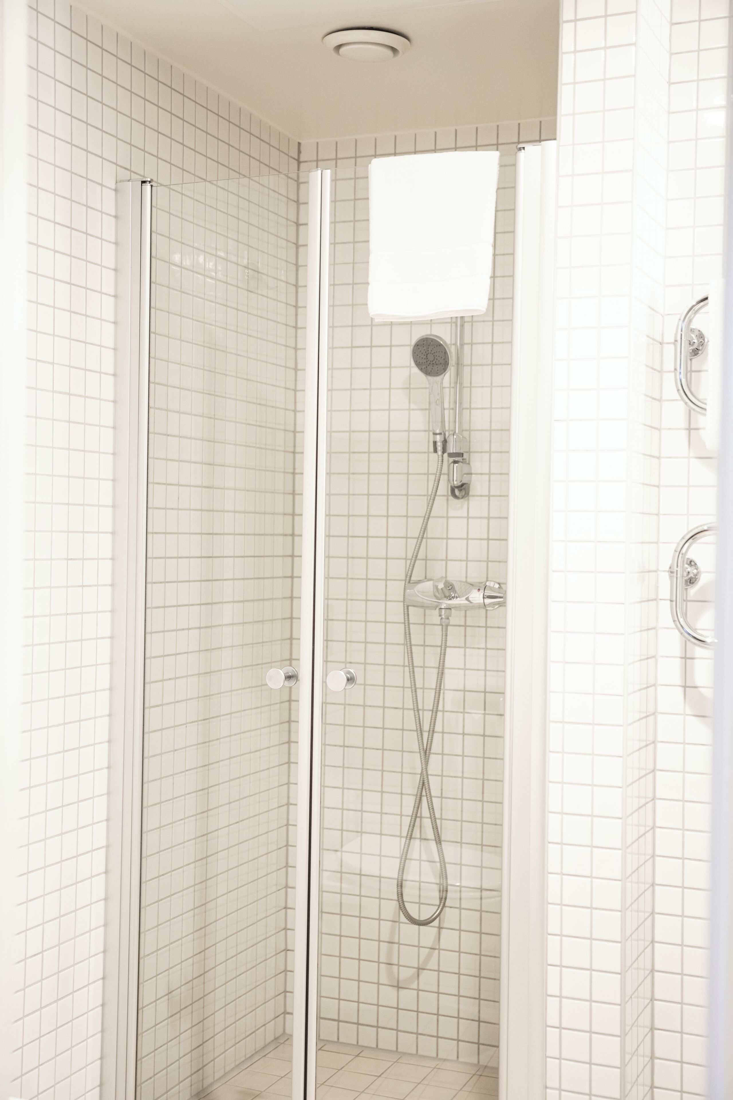 A glass-enclosed shower with a handheld showerhead and a wall-mounted faucet.