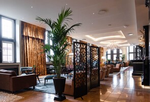 Un amplio vestíbulo de hotel con una planta en maceta grande, zonas de estar cómodas y un separador decorativo.