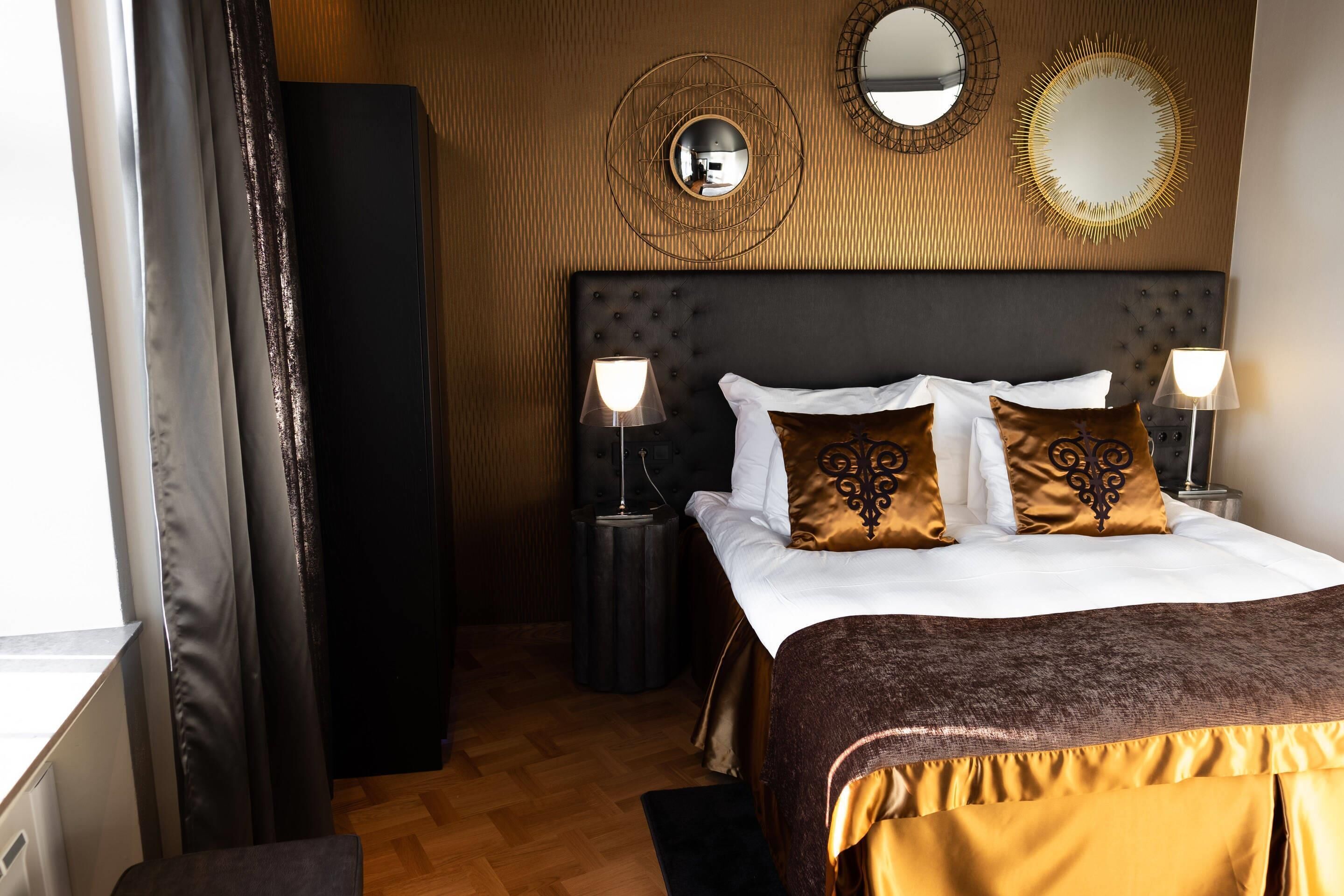 Habitación de hotel con una cama grande, dos lámparas de noche, un espejo redondo y un panel de pared de madera.