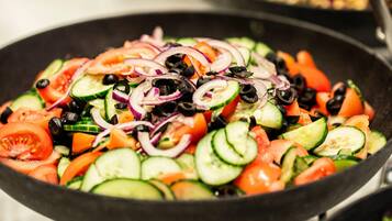 Primer plano de una ensalada de verduras colorida con tomates, pepinos, cebollas y aceitunas negras en una sartén.