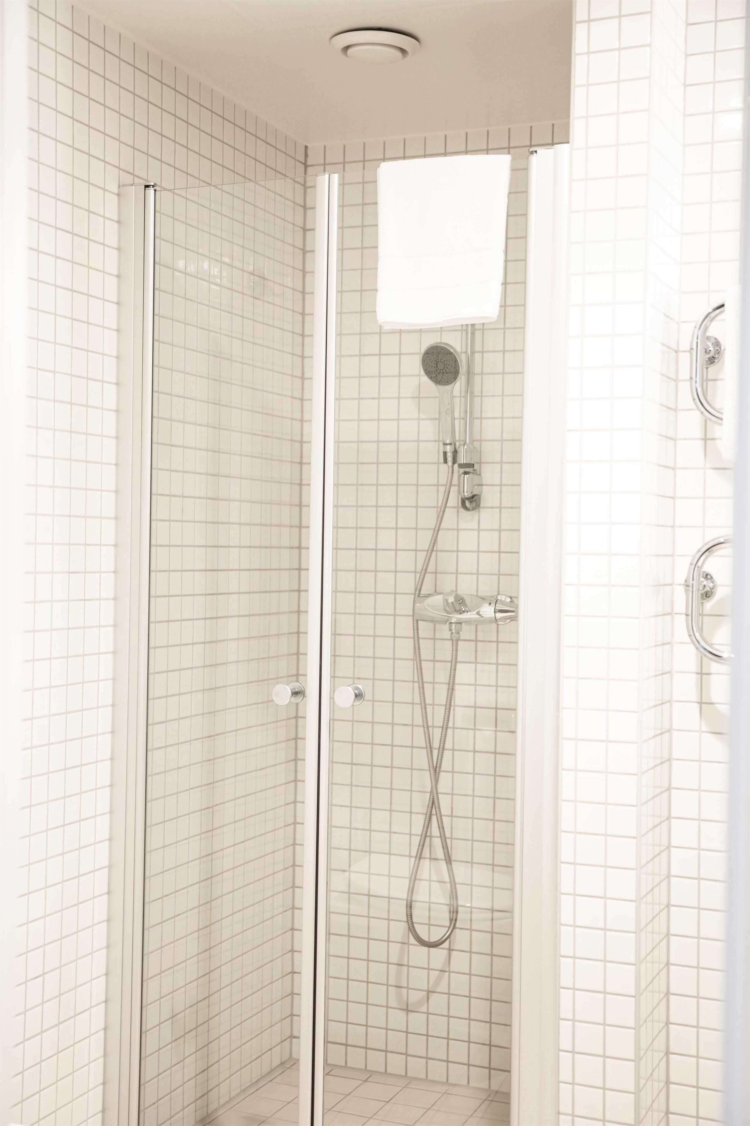 A glass-enclosed shower stall with a handheld showerhead and a wall-mounted faucet.