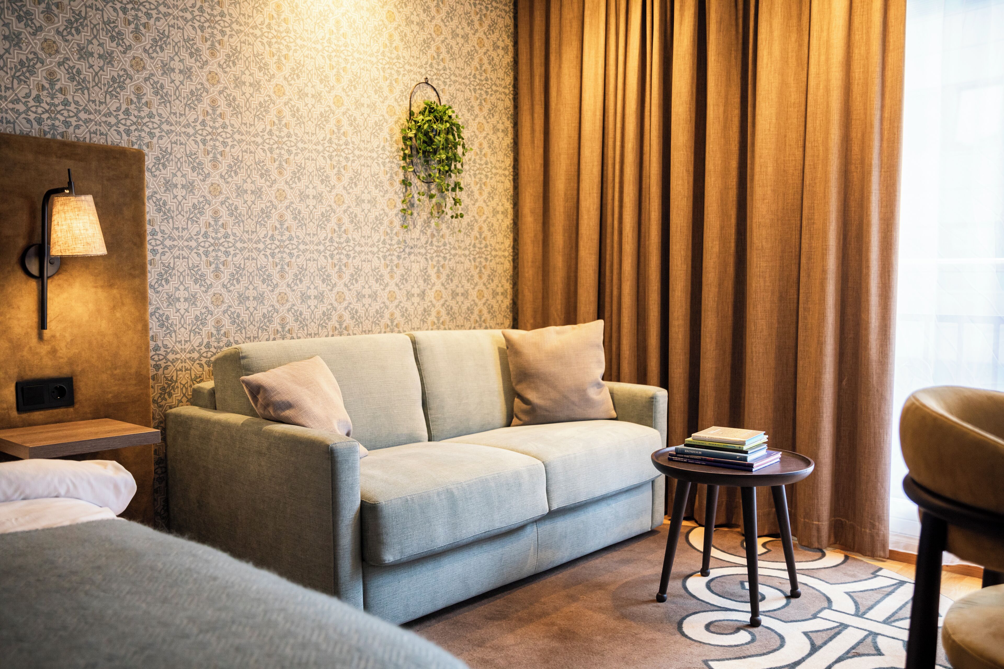 A modern hotel room with a sofa, a small table, a lamp, and a hanging plant.