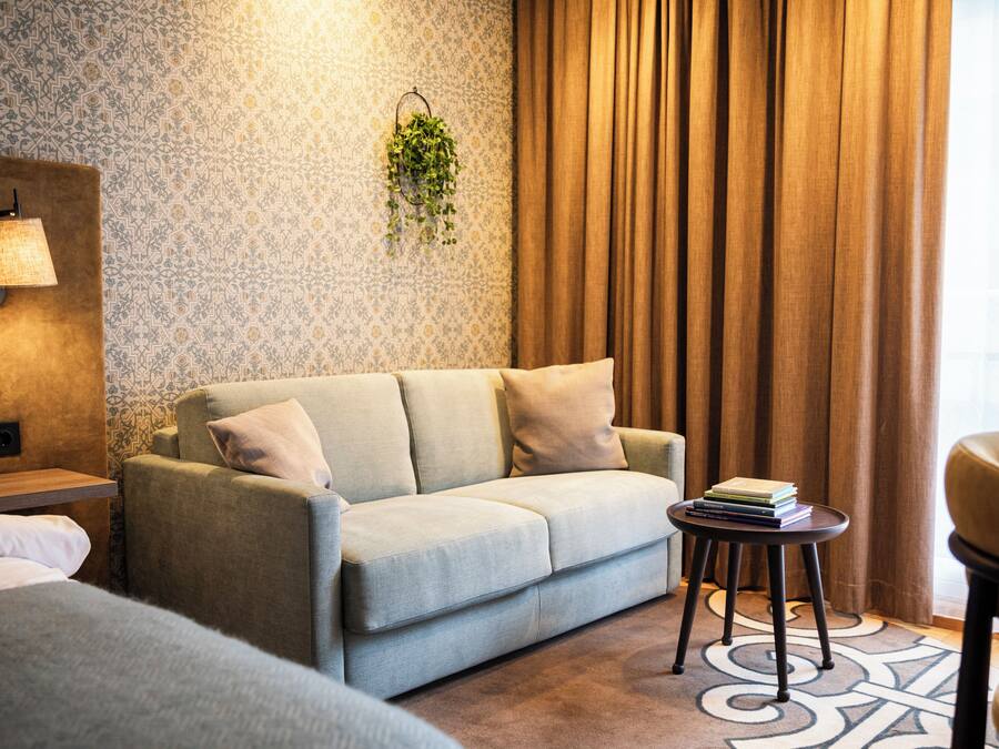 A modern hotel room with a sofa, a small table, a lamp, and a hanging plant.
