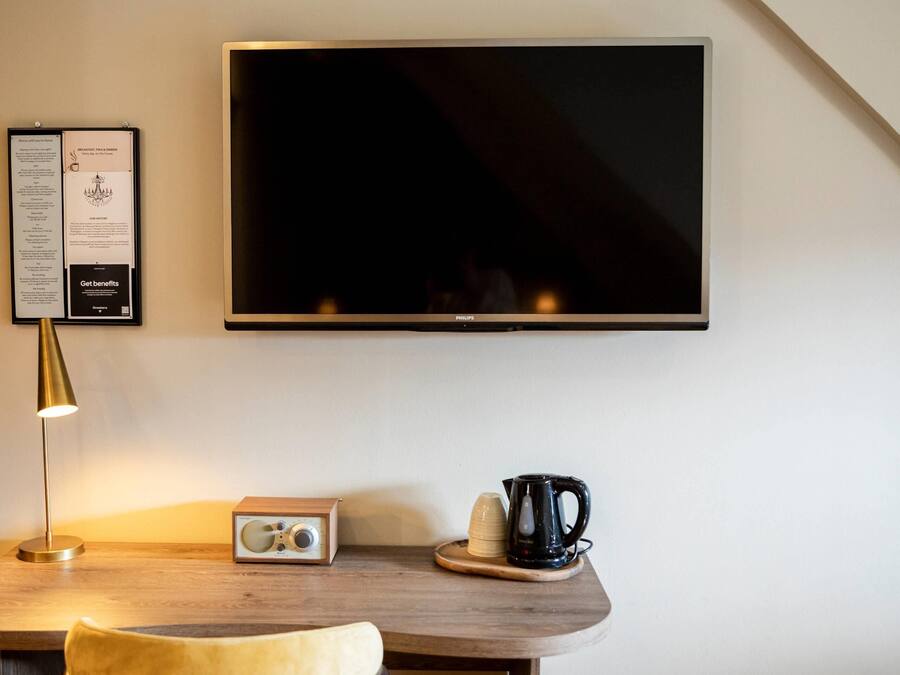 A modern room with a flat-screen TV mounted on the wall, a wooden table with a radio, a kettle, and a cup.