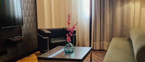 Una sala de estar moderna con un televisor de pantalla plana, un florero de cristal con flores, un sofá de cuero negro y una mesa de centro de madera.