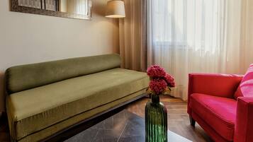 Een woonkamer met een groene bank, een rode fauteuil en een vaas met bloemen.