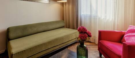 A living room with a green sofa, a red armchair, and a vase with flowers.