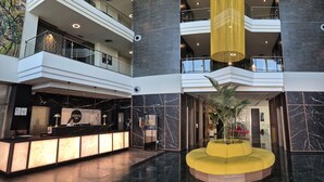 A modern hotel lobby with a reception desk, a central yellow seating area, and a high ceiling with a hanging light fixture. - Hotel Vértice Aljarafe (Bormujos)