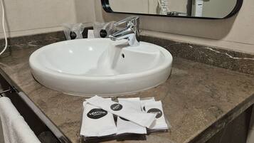 A white sink with a chrome faucet in a bathroom with a marble countertop. There are towels and toiletries on the counter.