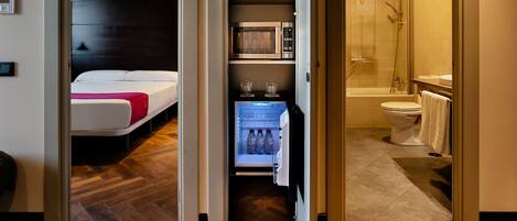 Habitación de hotel con cama, minibar, microondas y baño con ducha e inodoro.