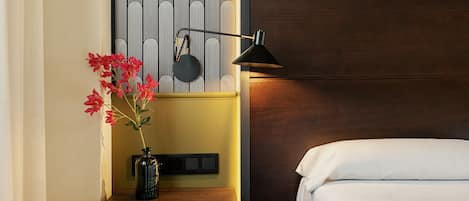 Habitación de hotel con cama, mesita de noche con un florero, lámpara y pared con estampado a rayas.