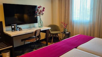 Ein Hotelzimmer mit einem Bett, einem Schreibtisch mit Stuhl, einem Fernseher und zwei Vasen mit Blumen.