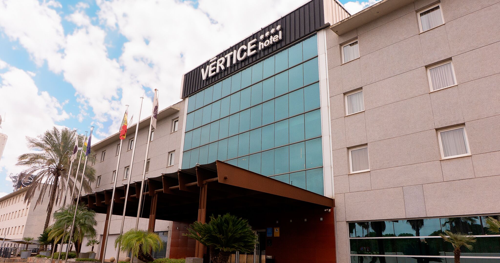 A modern hotel building with a prominent sign reading "VERTICE hotel".
