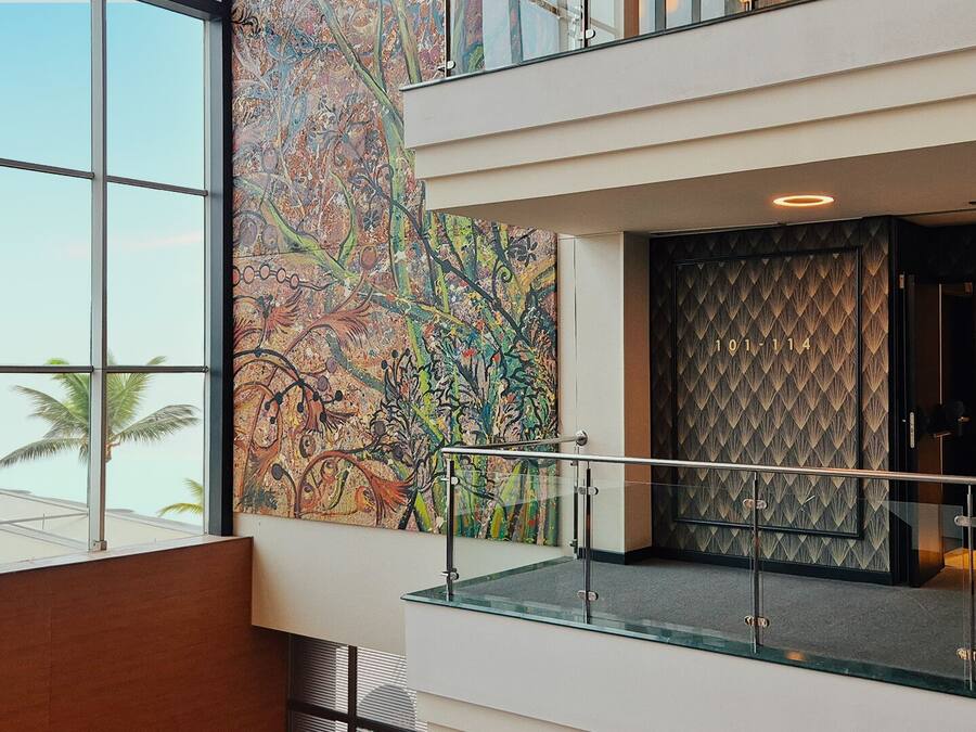 A modern hotel lobby with large windows, a colorful abstract mural, and a glass railing.