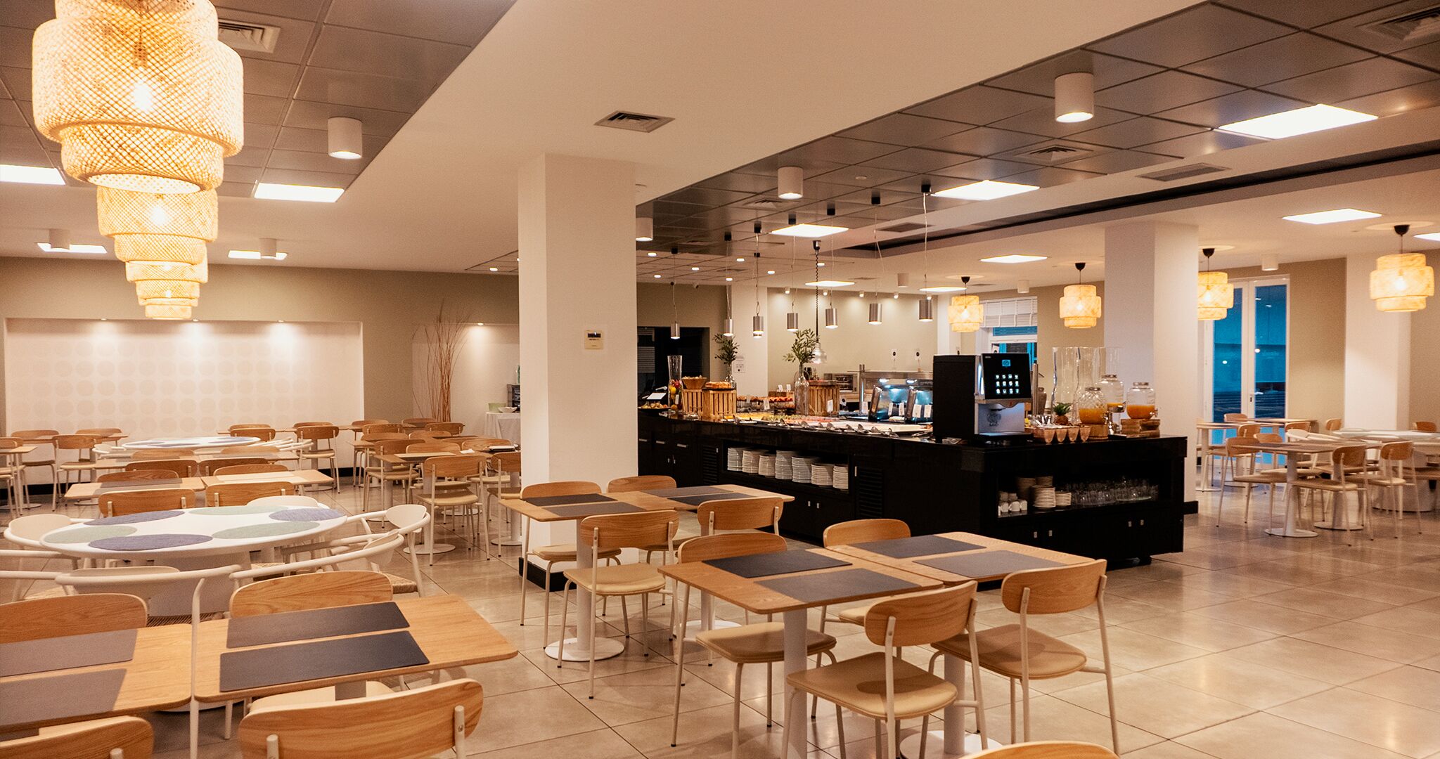 A spacious dining area with multiple tables and chairs, a central counter with a beverage station, and pendant lighting.