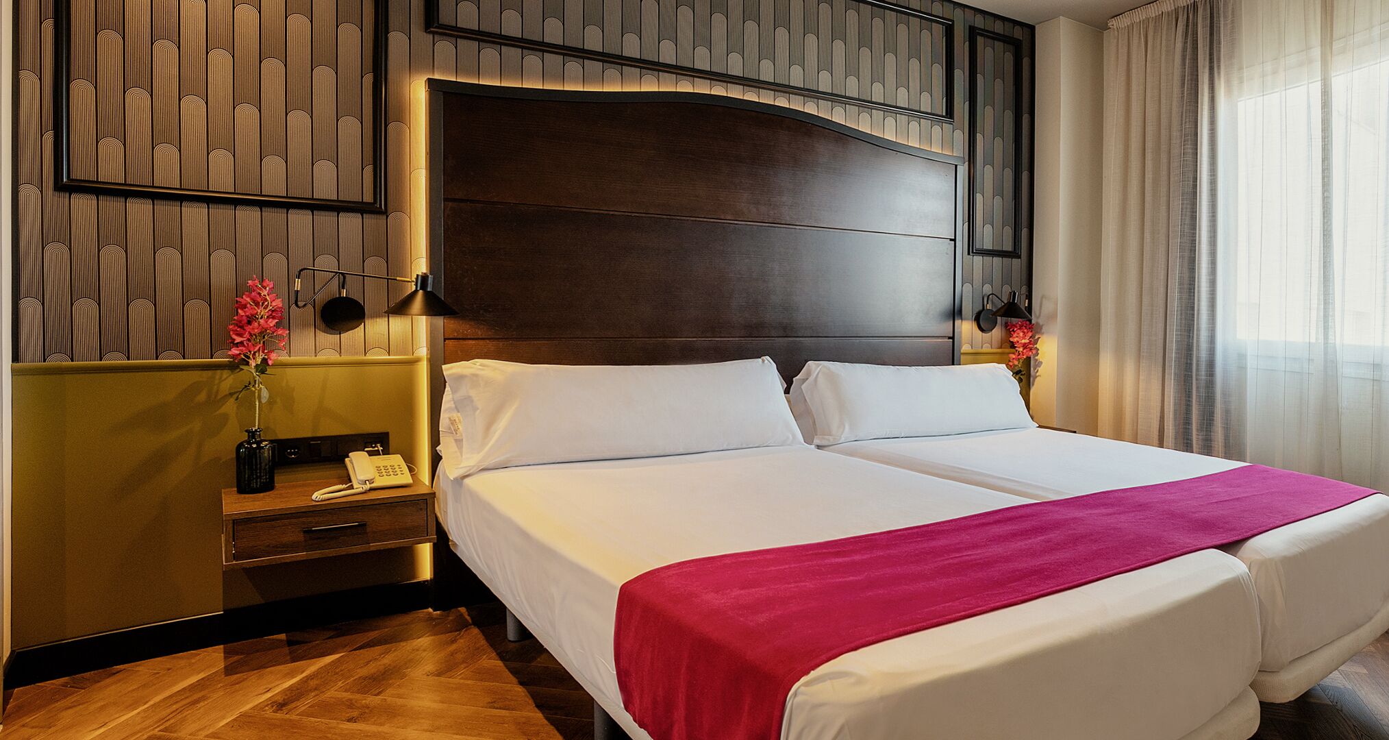 A hotel room with a large bed, a bedside table with a phone, and a wall with vertical paneling.