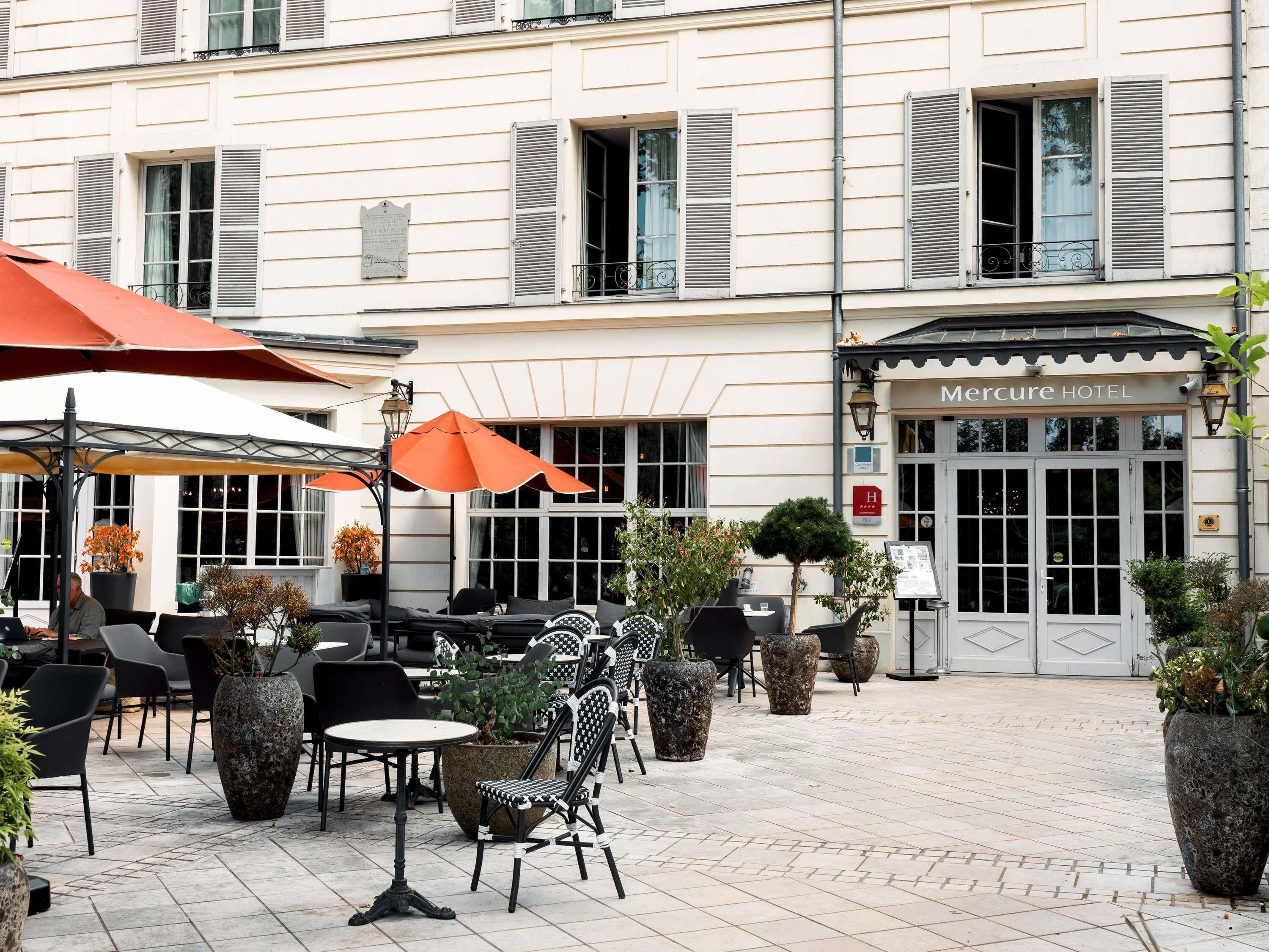 An outdoor seating area with tables and chairs, potted plants, and umbrellas at a hotel.