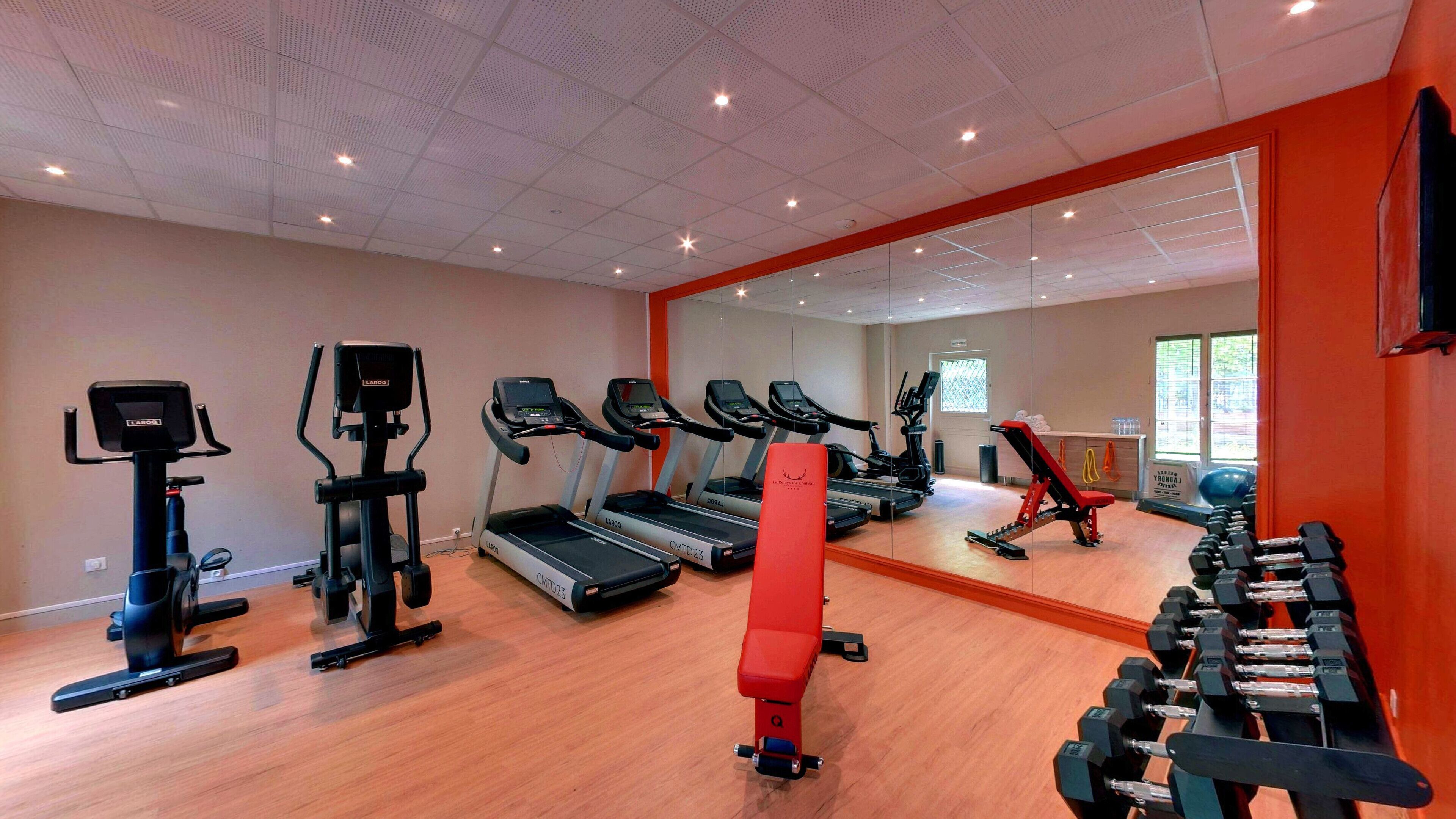 Un gimnasio con cintas de correr, elípticas, un banco rojo y mancuernas.