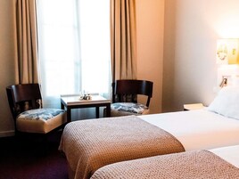 Una habitación de hotel con dos camas individuales, una mesita con una lámpara y dos sillas.