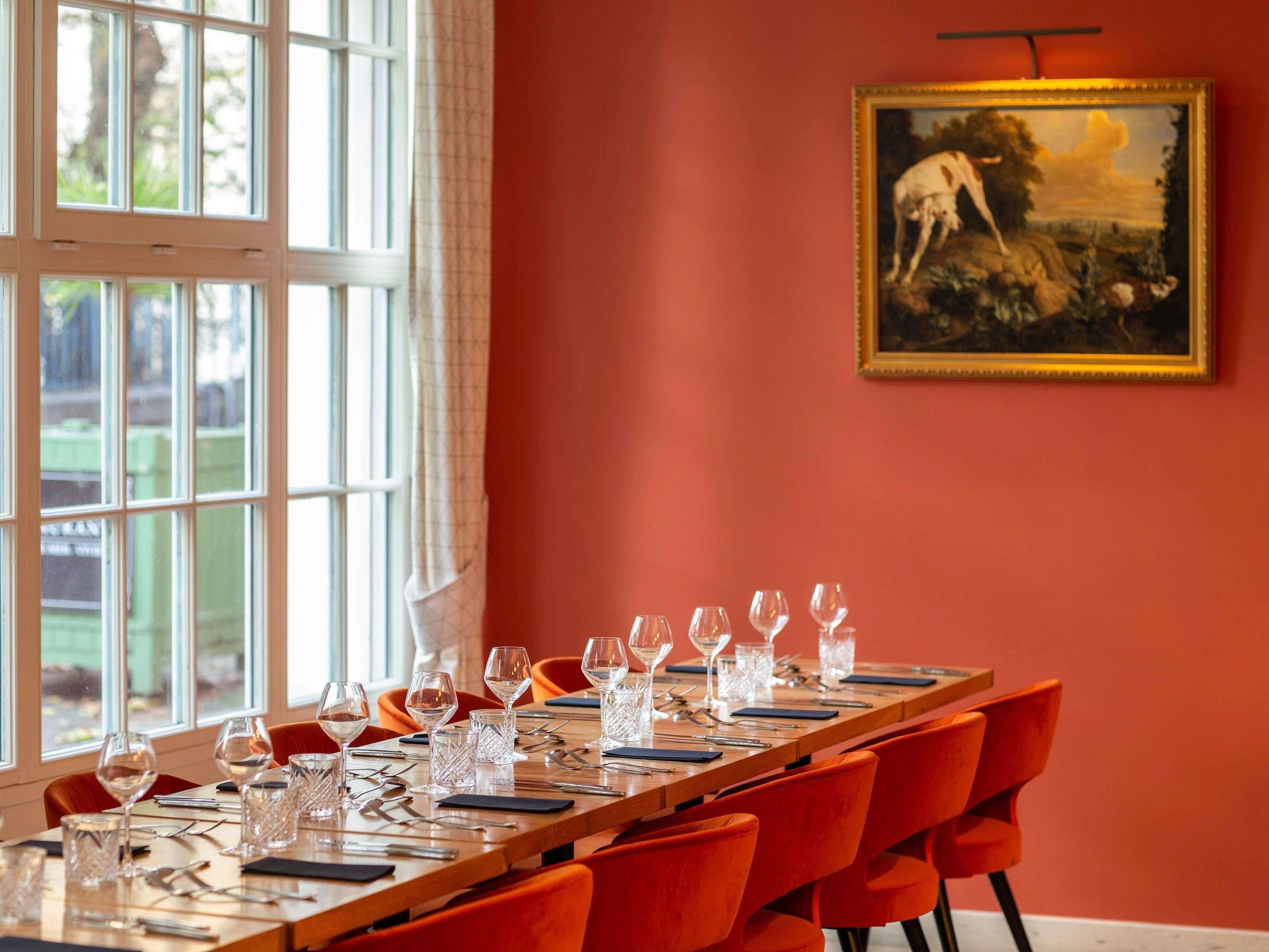 A dining area with a long table set for a meal, chairs, and a painting on the wall.